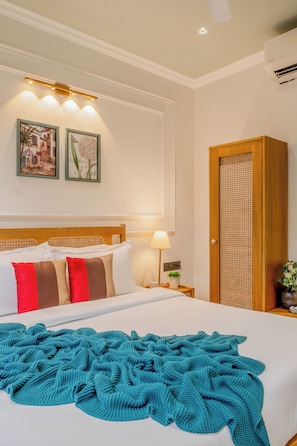 Habitación de hotel con cama, mesita de noche con lámpara, aire acondicionado en la pared y puerta con panel tejido.