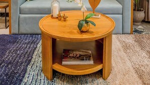Een woonkamer met een blauwe bank, een ronde houten salontafel en een decoratief wandobject.
