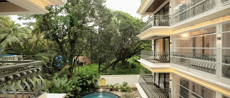 A multi-story hotel with a swimming pool surrounded by lush greenery.