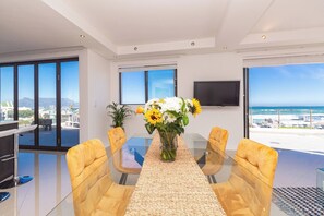 A modern dining area with a glass table, yellow chairs, and a vase of flowers. - Penthouse with the best view in Big Bay, Cape Town (Cape Town)