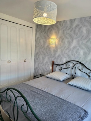 Een slaapkamer met een bed, nachtkastje, wandlamp en een kledingkast.