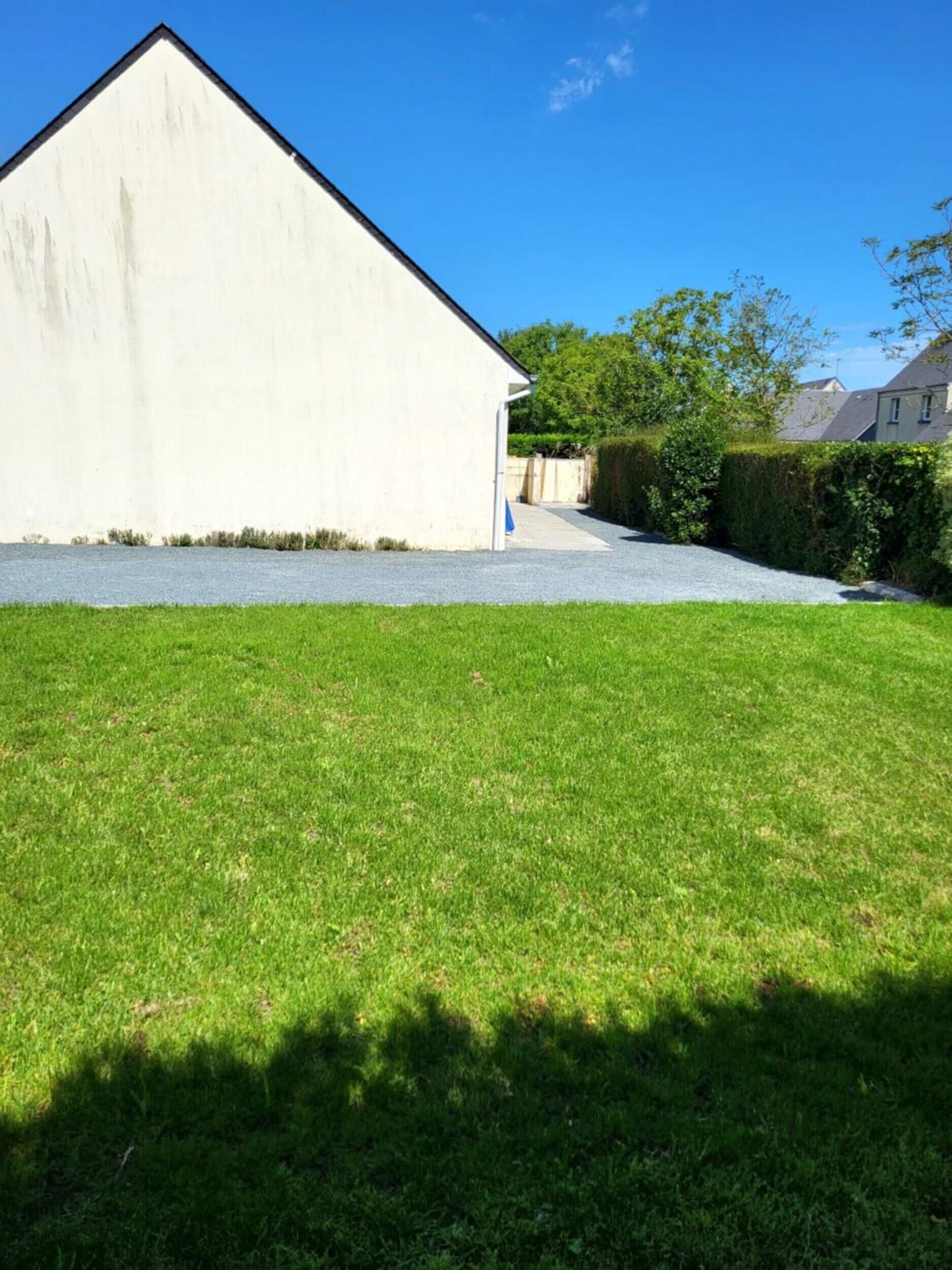 A white building with a sloped roof, a gravel driveway, and a well-maintained lawn.