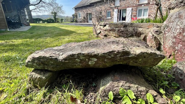 Une maison en pierre avec une cour verdoyante et une grande formation rocheuse.