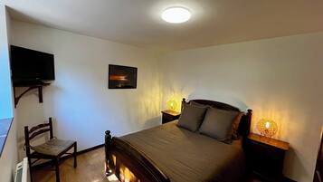 Een slaapkamer met een bed, een stoel, een aan de muur bevestigde televisie en een schilderij.