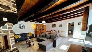 Un salon avec un mur en pierre, un plafond en bois, un canapé, une table basse et un coin repas comprenant des chaises et une table.