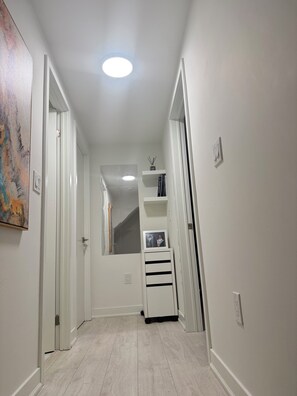 A hallway with white walls, a ceiling light, a door, and a shelf with a framed photo. - Havilah’s place for comfort and peace stay. Close to Donmil mall and recreation. (Toronto)