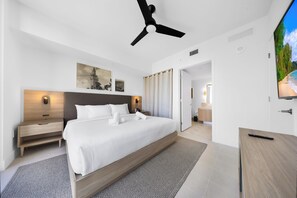 Ett modernt hotellrum med en stor säng, en takfläkt, en TV och ett nattduksbord i trä.