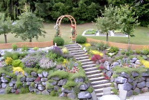 A garden with a stone staircase leading to an archway, surrounded by various plants and flowers. - Kleeblatt Apartment in West Allgäu with Private Terrace, Excellent Train/Bus Connections (Röthenbach (Allgäu))