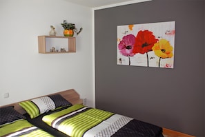 Un dormitorio con una cama, un estante en la pared con adornos, y una pintura floral.