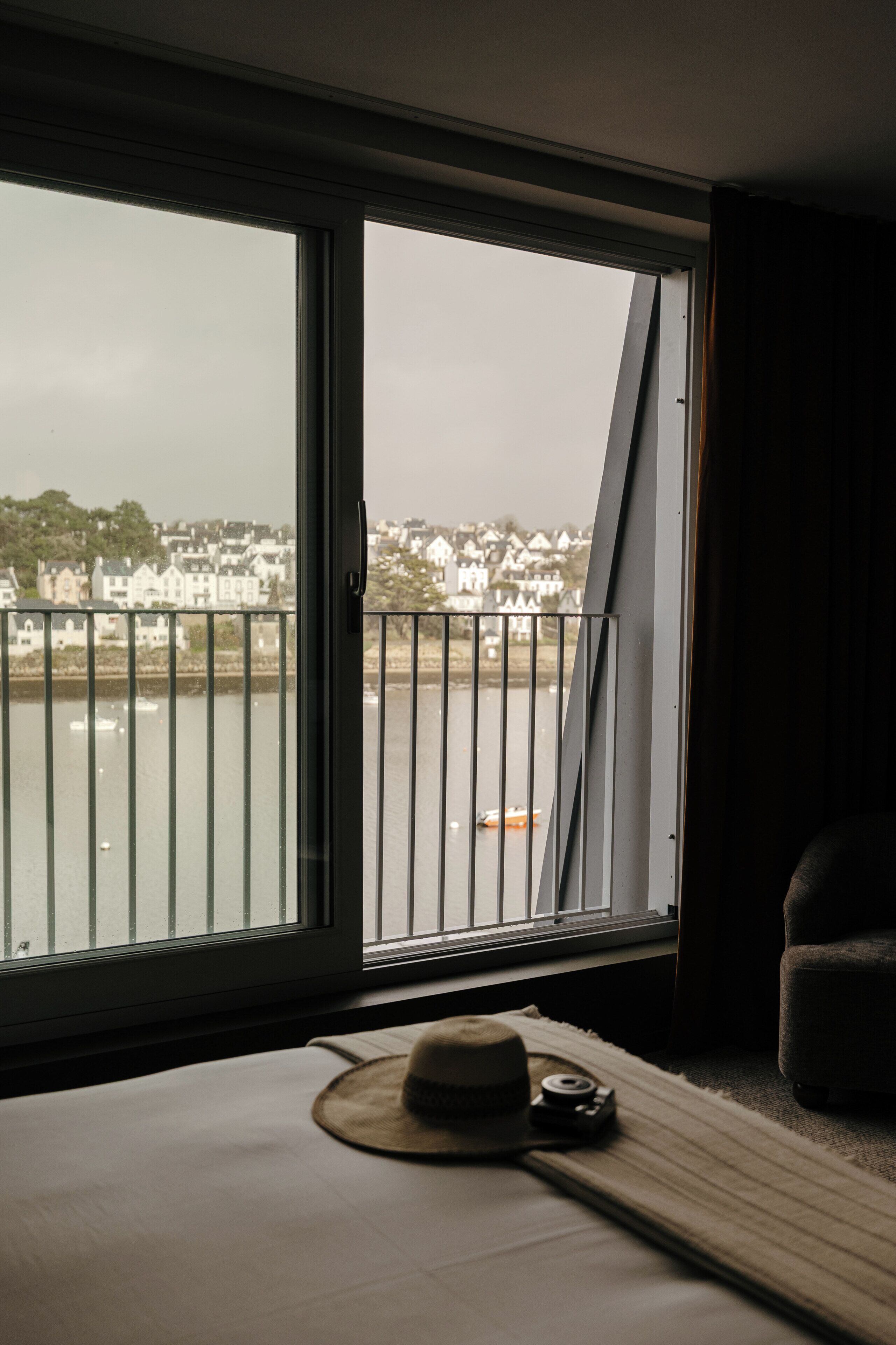 A room with a large window overlooking a body of water and a distant town.