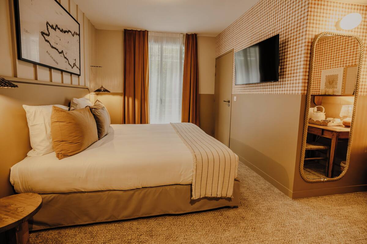 A hotel room with a bed, a mirror, a television, and a framed map on the wall.