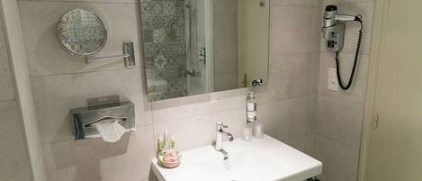 A bathroom with a white sink, a mirror, a towel rack, a hand dryer, and a soap dispenser.