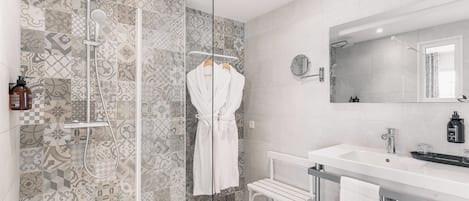 A modern bathroom with patterned tiles, a glass-enclosed shower, a white bench, and a large mirror.