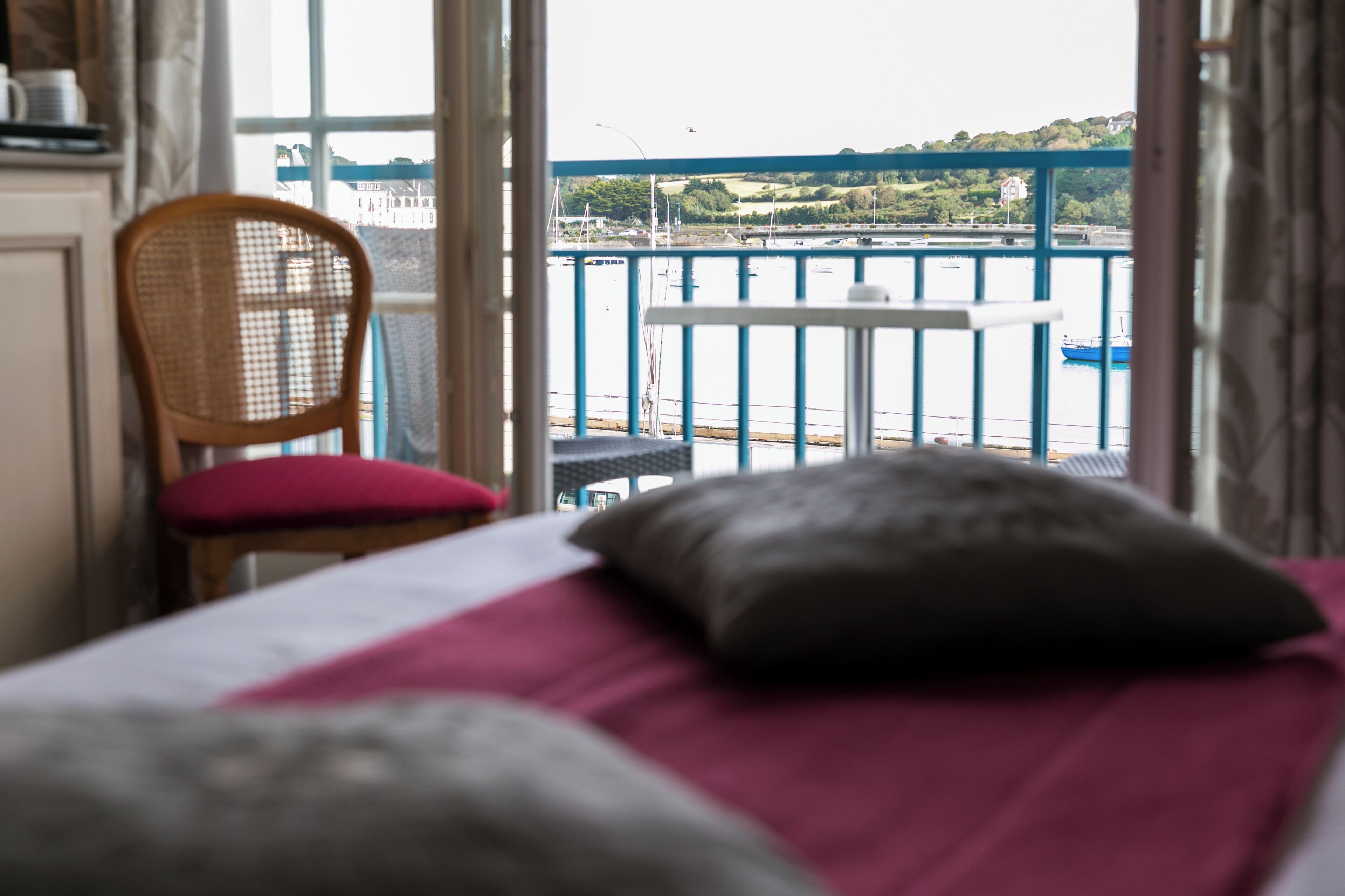 A room with a bed, a chair, and a view of a body of water with boats.