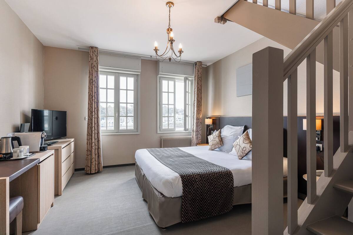 A hotel room with a bed, desk, TV, and a staircase.