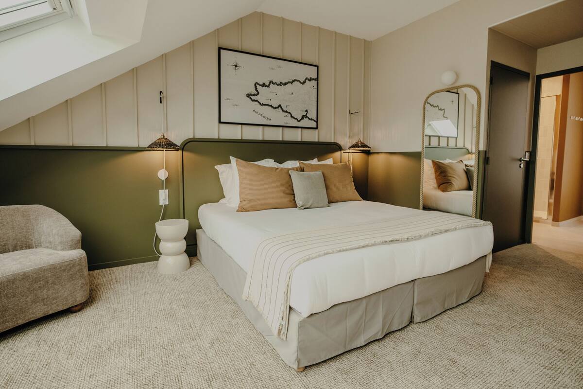 A bedroom with a bed, a chair, a map on the wall, and a mirror.