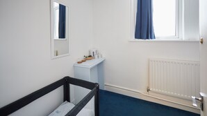 Ein Zimmer mit einem Babybett, einem Vorhangfenster, einer Heizung und einem kleinen Tisch mit Gegenständen darauf.