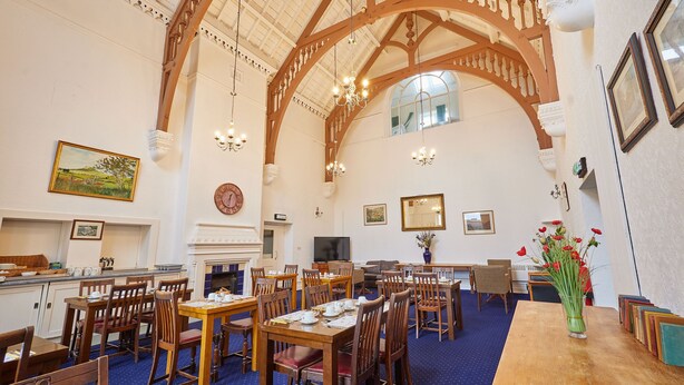 A spacious dining area with wooden tables and chairs, a fireplace, and a large window. - Saltburn House Hotel Double Rooms (Redcar and Cleveland)