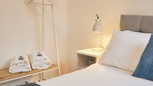 A neatly made bed with white linens, a bedside lamp, and a small shelf with folded towels. - Saltburn House Hotel Double Rooms (Redcar and Cleveland)