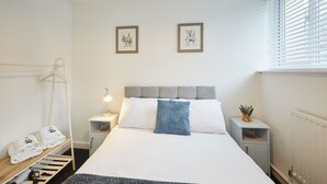 A neatly arranged hotel room with a bed, bedside tables, a hanging coat rack, and a small shelf with towels. - Saltburn House Hotel Double Rooms (Redcar and Cleveland)