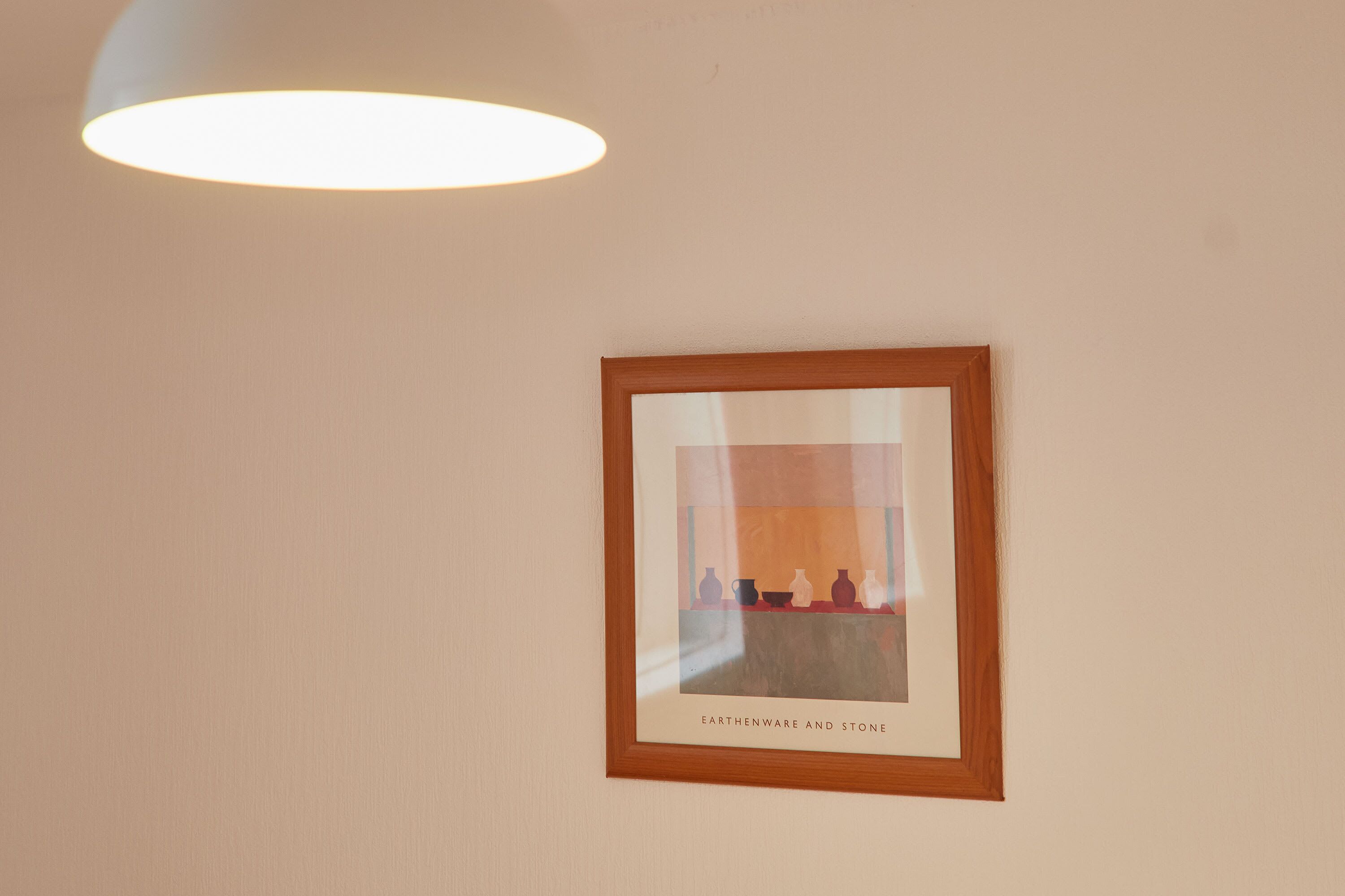 Een lijstwerk met daarin een kunstwerk getiteld 'EARTHENWARE AND STONE' aan een muur.