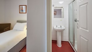 Een hotelkamer met een bed, een nachtkastje, een wit wastafelmeubel en een douchecabine van glas.