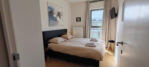 A bedroom with a bed, a radiator, a window with curtains, and a painting on the wall. - Zeebrugge Sea View Apartment, Steps to the Beach (Brugge)