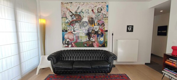 A living room with a black leather sofa, a colorful abstract painting on the wall, and a patterned rug. - Zeebrugge Sea View Apartment, Steps to the Beach (Brugge)