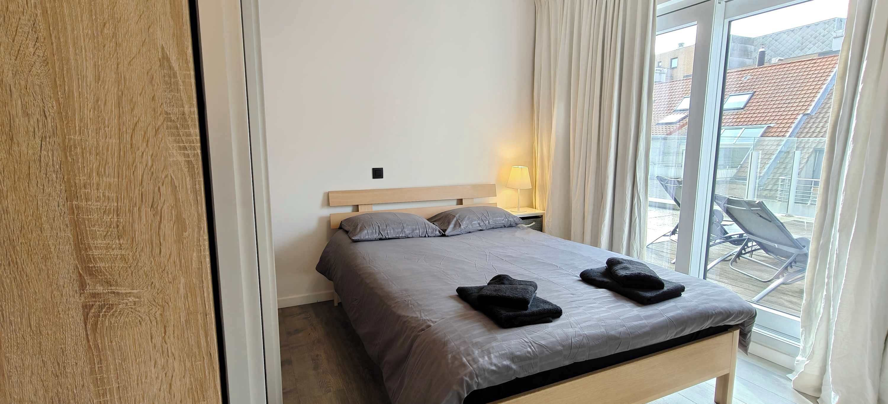 Habitació d'hotel amb un llit, una tauleta de nit amb una làmpada, una finestra amb cortines i vista a l'exterior.