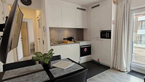 Eine kompakte Küche mit Mikrowelle, Backofen und Spüle, ein Essbereich mit Tisch und Stühlen sowie eine Glastür zum Außenbereich.