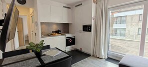 A compact kitchen with a microwave, oven, and sink, a dining area with a table and chairs, and a sliding glass door to the outside. - Beachfront Knokke Apt w/ Panoramic Terrace Views (Knokke-Heist)