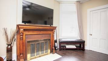 A living room with a fireplace, a television mounted above it, a bench, and a door.