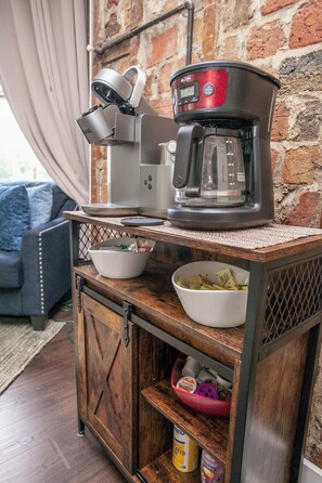 A coffee maker on a wooden cabinet with a brick wall in the background.