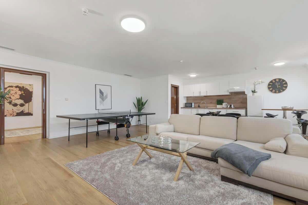 Una sala de estar moderna con una mesa de centro de vidrio, un sofá, una mesa de comedor con sillas y una cocina al fondo.