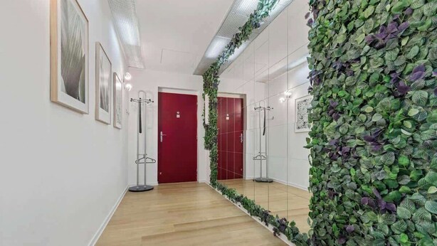 A hallway with a wooden floor, a red door, and a wall covered with green foliage. - Family Hub in Centre (Bratislava - Old Town)