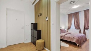 Un dormitorio con cama, armario, un taburete pequeño y una pared con líneas verticales.