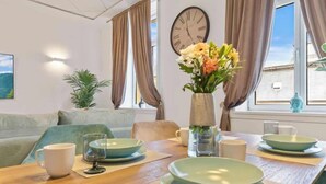 Un comedor con una mesa dispuesta para cuatro, un reloj en la pared y vistas al exterior.