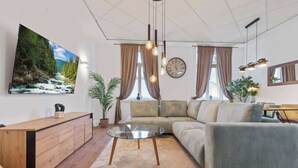 Una sala moderna con un sofá, una mesa de centro de cristal, un aparador de madera, un cuadro grande, un reloj y una planta en maceta.