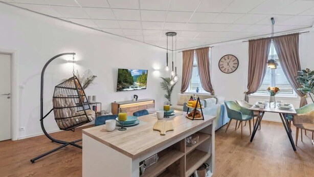 Una sala moderna con comedor, una silla colgante, una mesa de centro de madera y un reloj en la pared.
