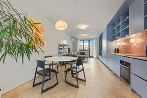 Eine moderne Küche mit blauen Schränken, ein Essbereich mit einem runden Tisch und eine große Pflanze.