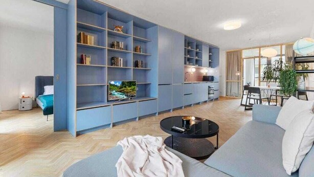 A modern living room with a large blue bookshelf, a sofa, a coffee table, and a TV.