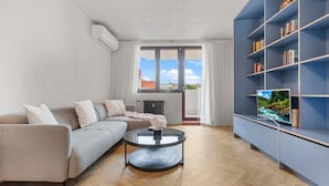A modern living room with a sofa, a round coffee table, and a bookshelf with a television.