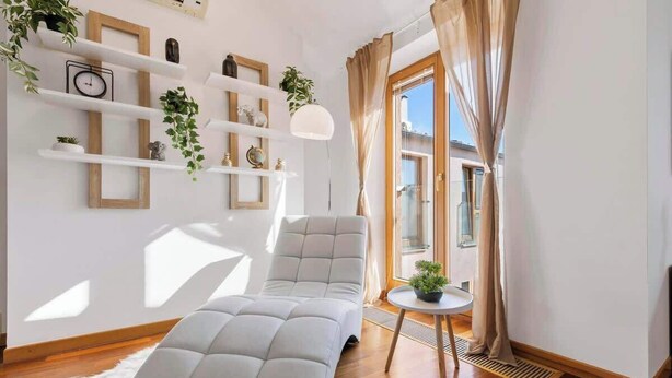 A modern living room with a sofa, a small round table with a plant, and a window with curtains.