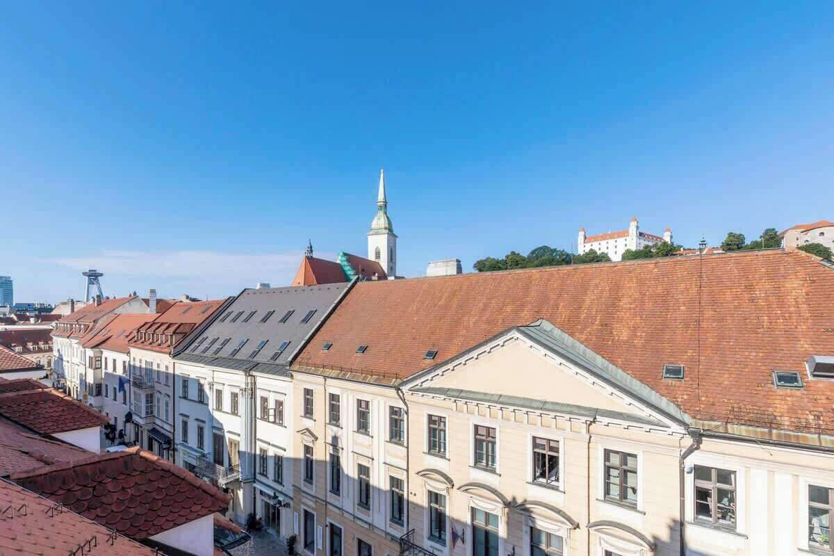 A row of historic buildings with red-tiled roofs and a prominent church spire.