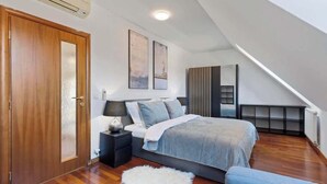 A bedroom with a bed, a nightstand, a white furry rug, and a wooden door.