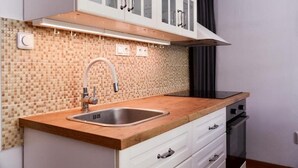 A kitchen with a tiled backsplash, a stainless steel sink, wooden countertop, white cabinetry, and a black range hood.