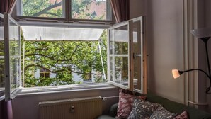 A room with a large window, a radiator, a sofa with patterned cushions, and a floor lamp.