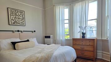 A bedroom with a bed, a dresser, a radiator, and a window with curtains.