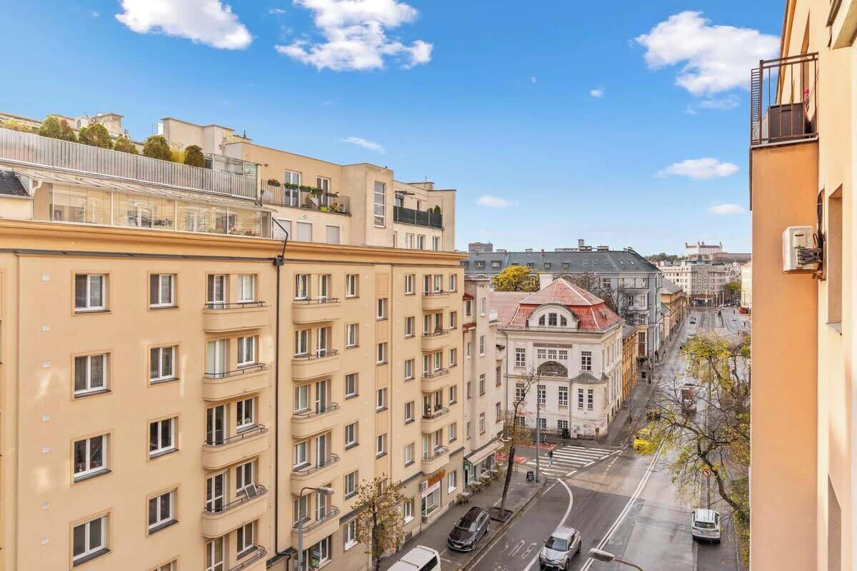 A multi-story building with balconies, a street view, and a clear sky.