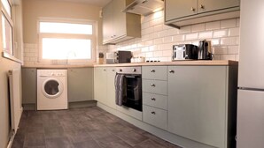 A compact kitchen with a washing machine, oven, and a window providing natural light. - 4 Bed • Parking • Near M4 • Ideal for Workers (Aberavon)